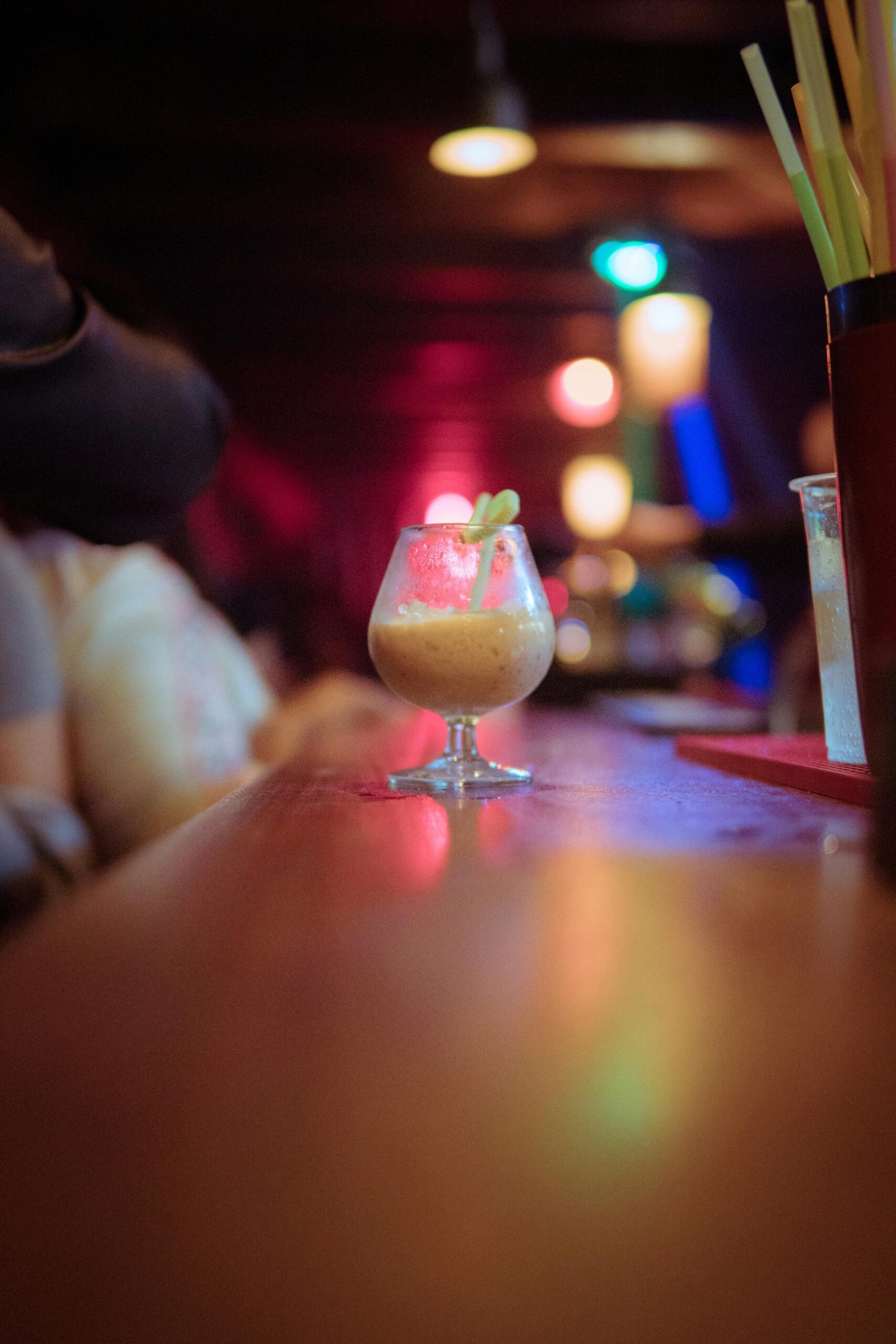 A vibrant cocktail on a bar counter with colorful lighting and lively atmosphere.