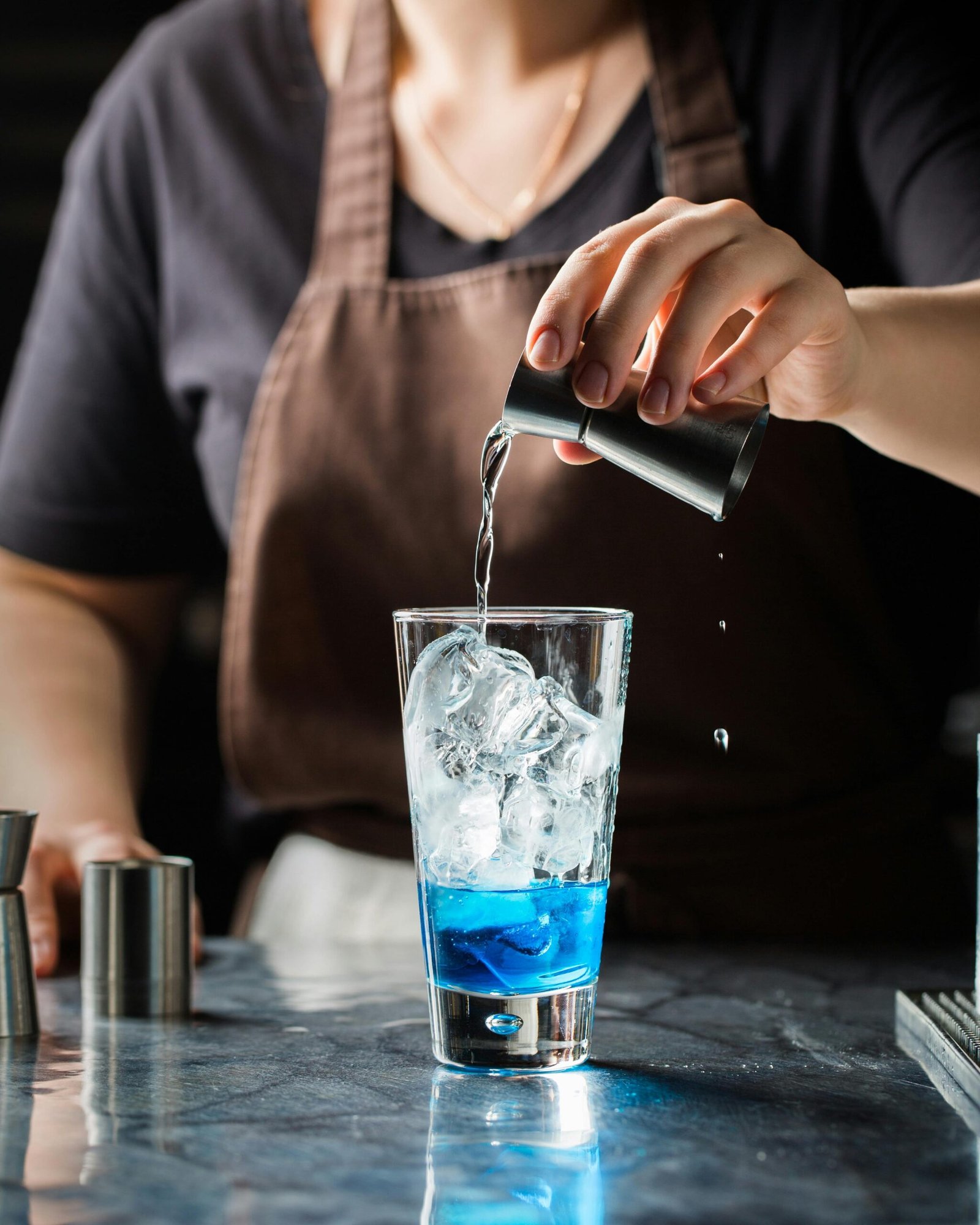 A bartender pouring a refreshing blue cocktail over ice in a glass.