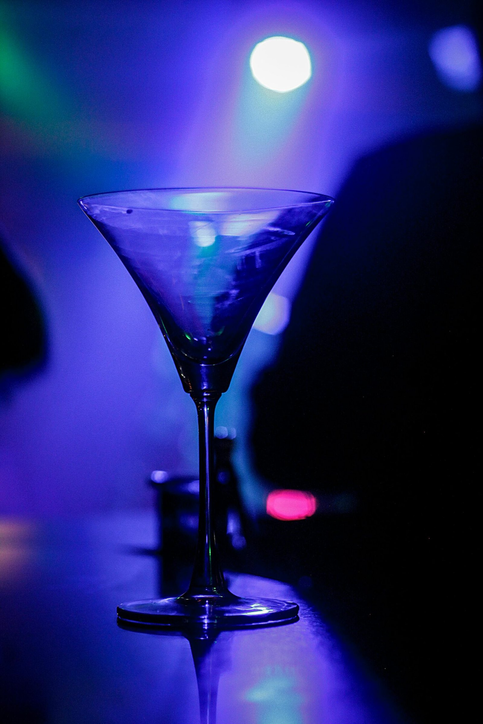 A crystal martini glass glows under vibrant nightclub lighting.