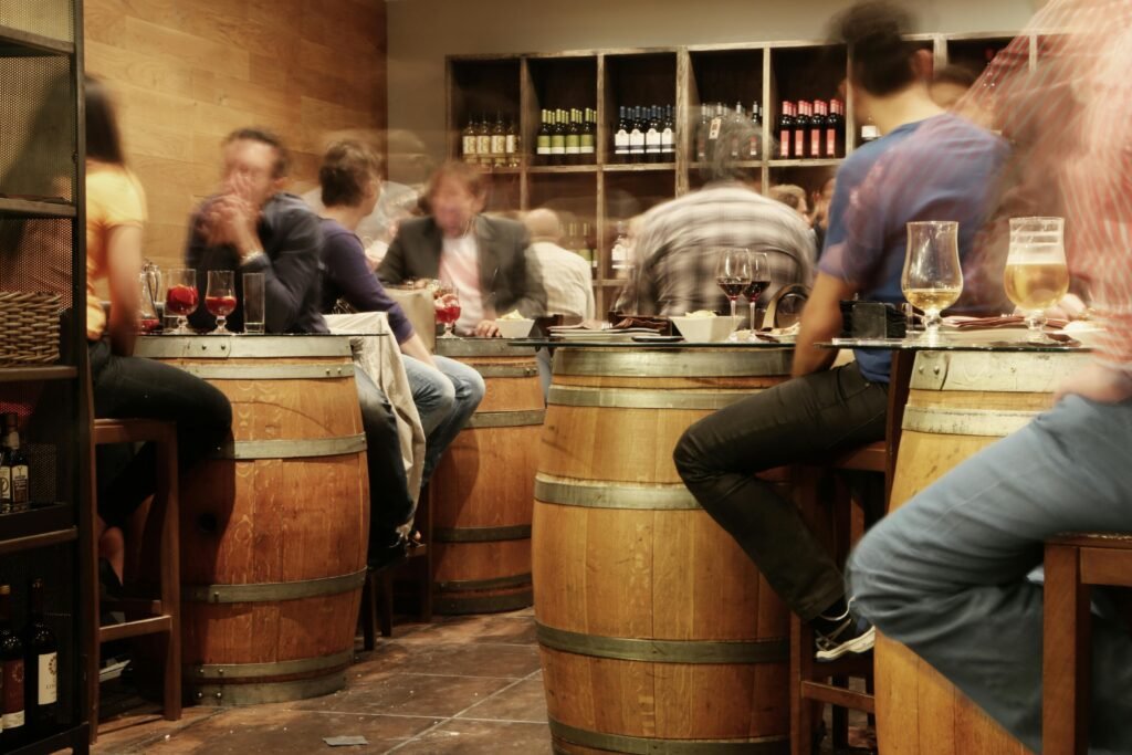 Lively bar setting with people enjoying drinks and tapas around wine barrel tables.